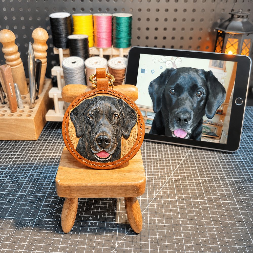 Handcrafted round leather keychain featuring a custom portrait of a black Labrador, displayed beside the pet’s reference photo on a tablet.