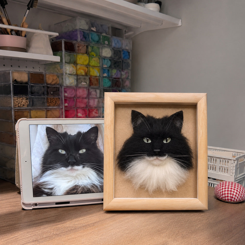 Handmade 3D felt portrait of a black and white long-haired cat displayed in a natural wood frame beside the pet’s reference photo.