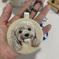 Custom round embroidered portrait keychain featuring a small light-brown dog on beige fabric with a silver-tone clasp.