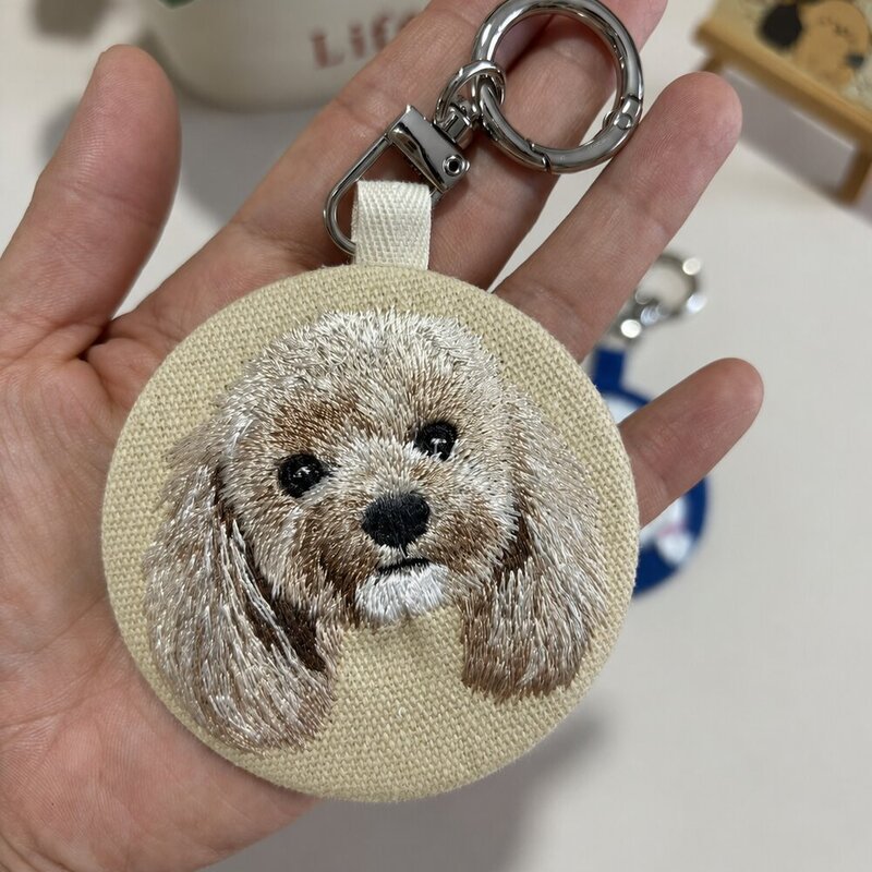 Custom round embroidered portrait keychain featuring a small light-brown dog on beige fabric with a silver-tone clasp.