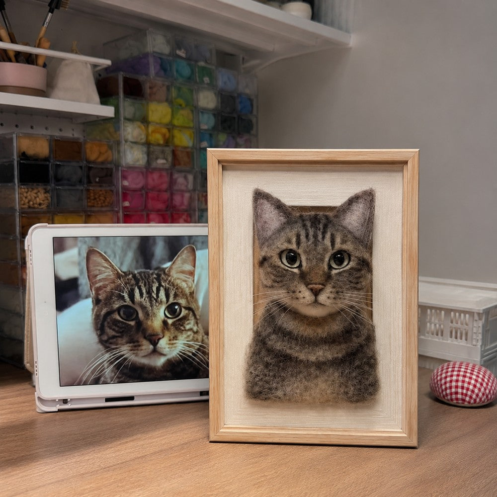 Handmade full-body 3D felt portrait of a brown tabby cat displayed in a natural wooden frame beside the cat’s reference photo.