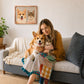 Woman holding a Corgi and tabby cat beneath their custom glass pet portrait in a cozy living room.