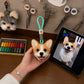 Handmade Corgi head bag charm with a green hanging loop displayed beside the dog’s reference photo in an artisan workshop.