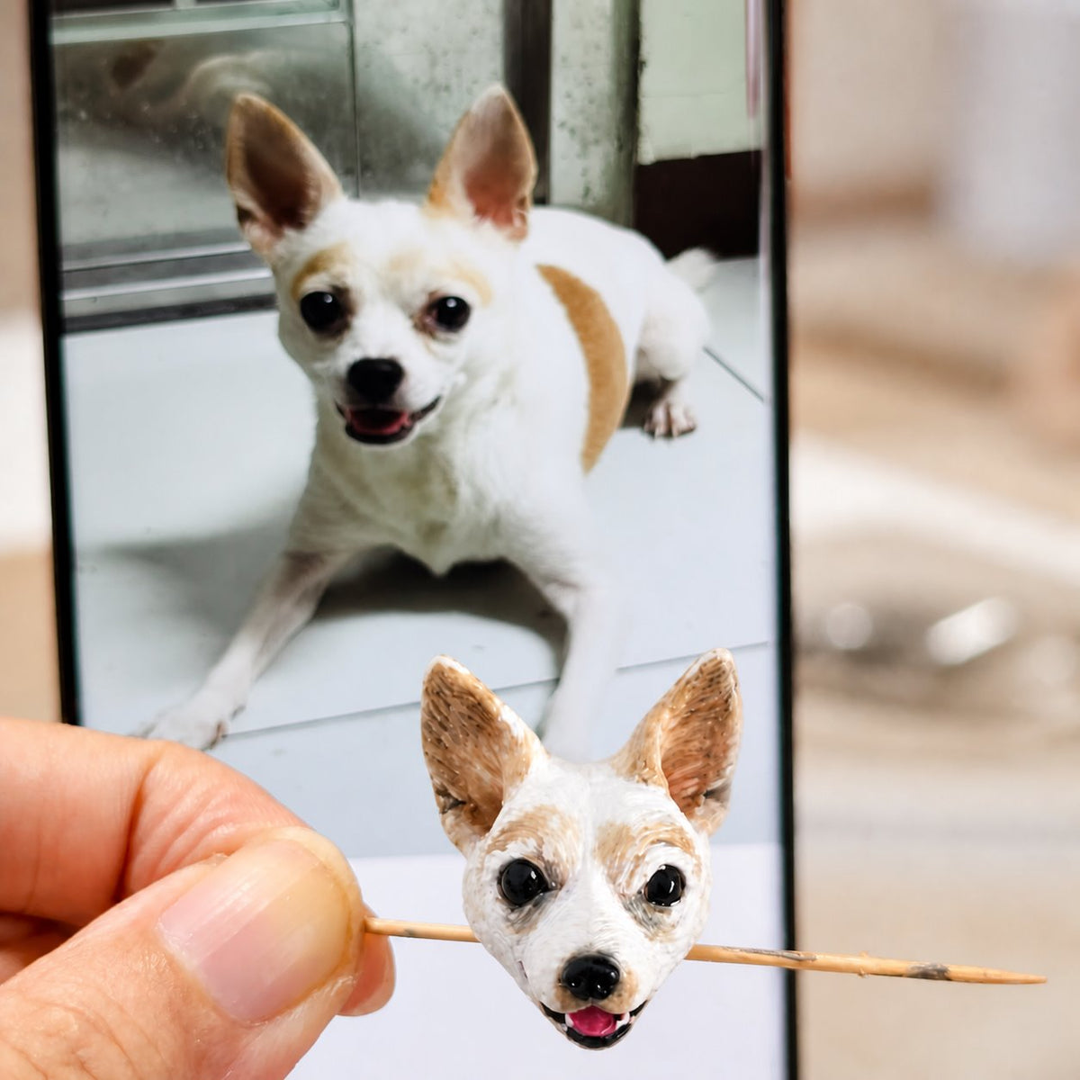 Artist hand-painting a custom dog portrait bracelet charm beside the pet's phone reference photo.