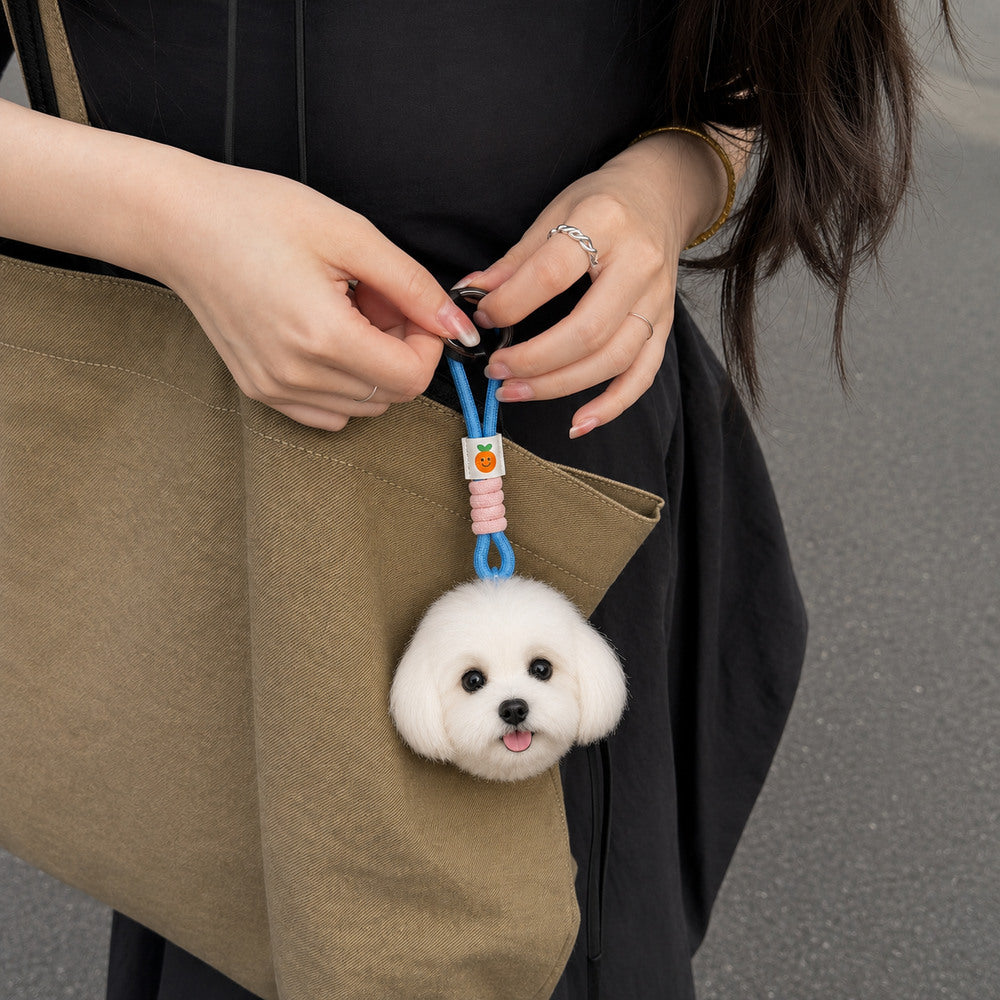 Woman attaching a personalized white dog head charm with a blue hanging loop to an olive canvas tote bag.