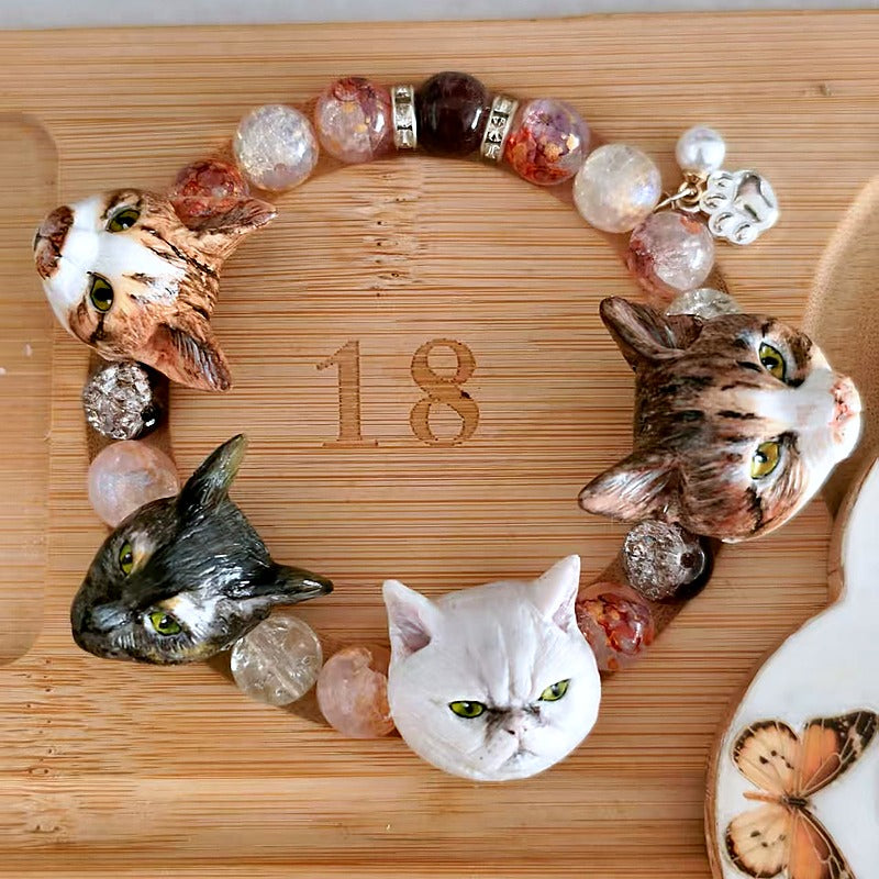 Close-up of a custom four-cat portrait bracelet with hand-sculpted cat face charms and pink crystal beads.