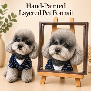 Gray dog in a navy striped shirt beside its custom hand-painted layered pet portrait in a dark frame on a wooden easel.
