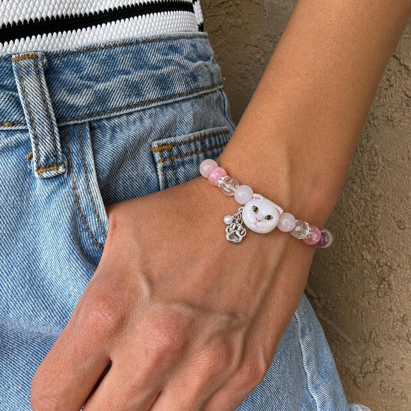 Personalized white folded-ear cat portrait bracelet worn with pink and purple crystal beads.