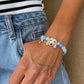 Personalized cream long-eared dog portrait bracelet worn on the wrist with bright blue and aqua beads.