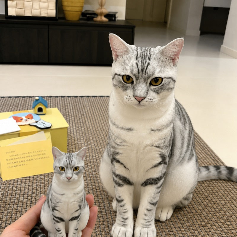 Hand holding a custom silver tabby cat figurine beside the real cat used as the reference.