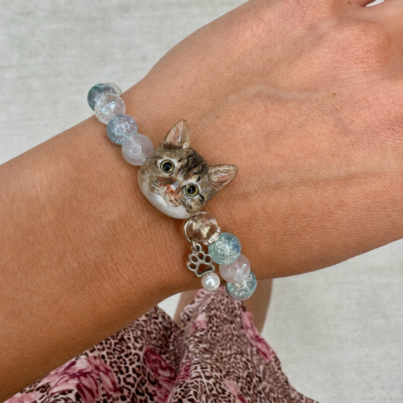 Custom tabby cat portrait crystal bracelet worn on the wrist with a hand-sculpted cat face charm and blue beads.