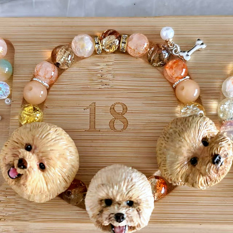 Custom three-dog portrait bracelet with hand-sculpted fluffy dog face charms and warm pink crystal beads.