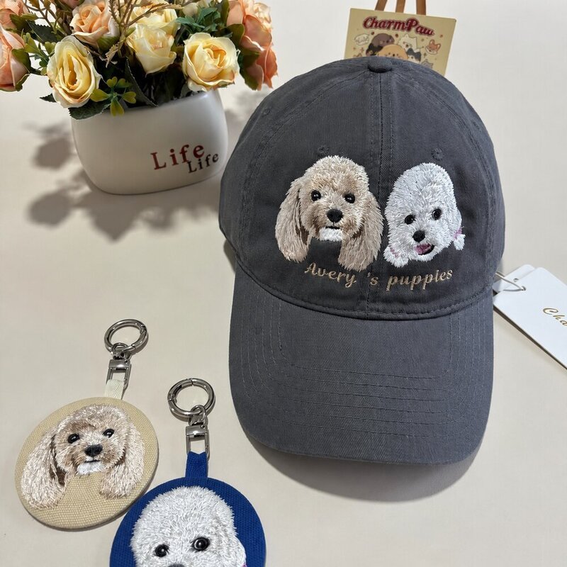 Custom dark gray cap embroidered with two small dog portraits, displayed with matching personalized round pet portrait keychains.