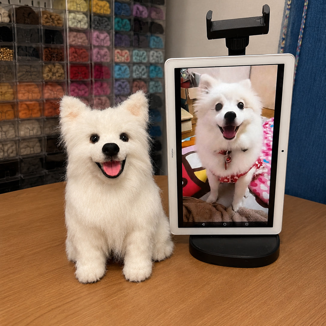Lifelike handmade replica of a smiling white Spitz dog displayed beside the customer’s reference photo on a tablet.