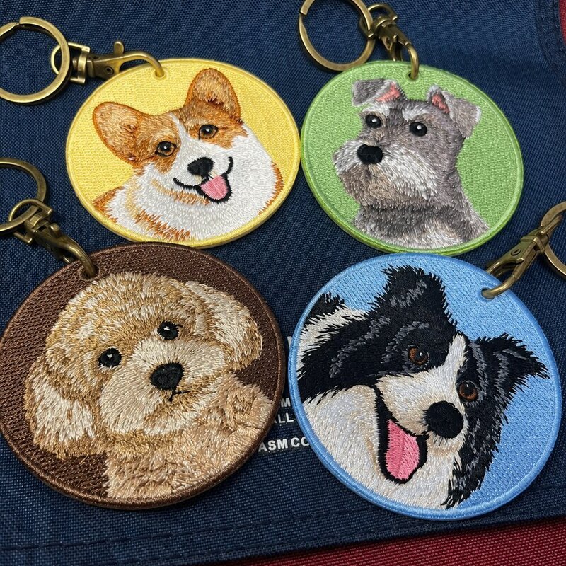 Four custom round embroidered dog portrait keychains featuring different breeds and colorful fabric backgrounds.