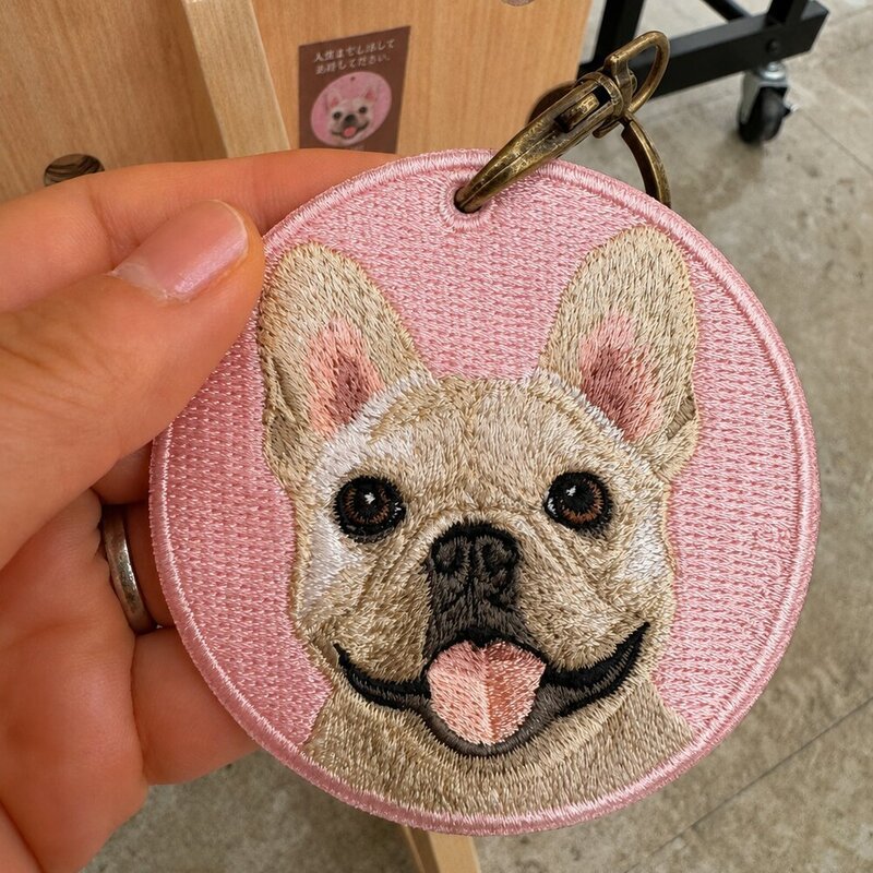 Custom round embroidered French Bulldog portrait keychain with a pink fabric background and antique brass-tone clasp.