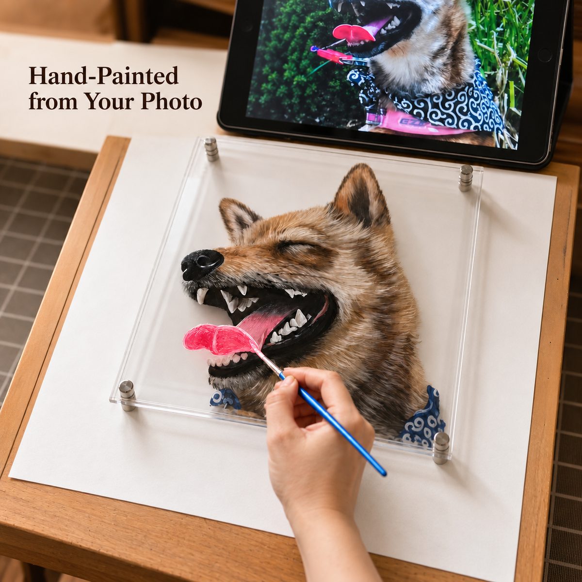 Hand-painted pet portrait in progress, with a brush adding tongue details and the dog's reference photo on a tablet.