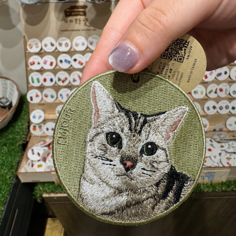 Custom round embroidered gray tabby cat portrait keychain with an olive green fabric background and antique brass-tone ring.