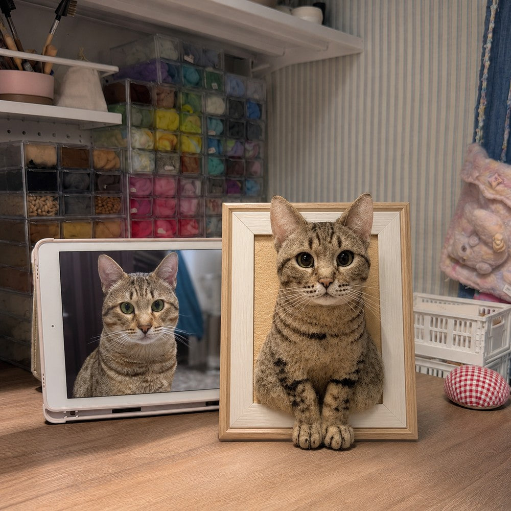 Handmade full-body 3D felt portrait of a brown tabby cat displayed in a wooden frame beside the cat’s reference photo.