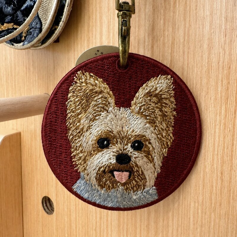 Custom round embroidered Yorkshire Terrier portrait keychain on a burgundy fabric background with antique brass-tone hardware.